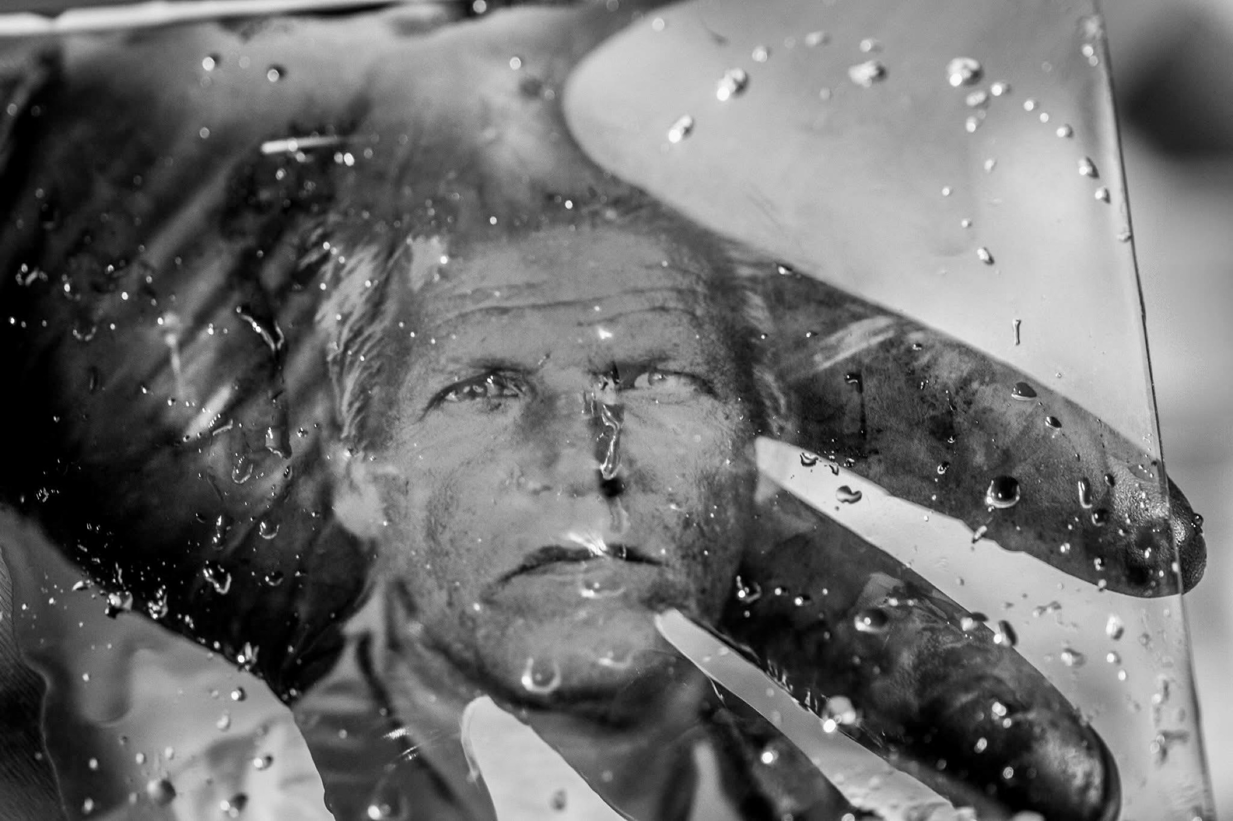 A layered black and white self-portrait seen through rain and reflections